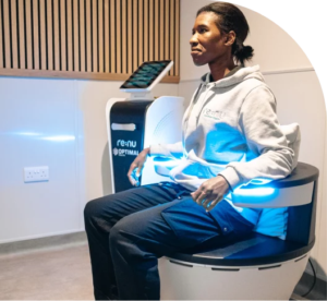 Angled view of a woman sitting in Re:nu London's electromagnetic pelvic floor therapy chair emitting a cool blue light.