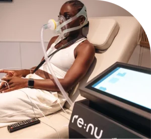 A woman sitting in a comfortable treatment bed wearing a specialist hypoxic therapy mask with Re:nu equipment in the foreground