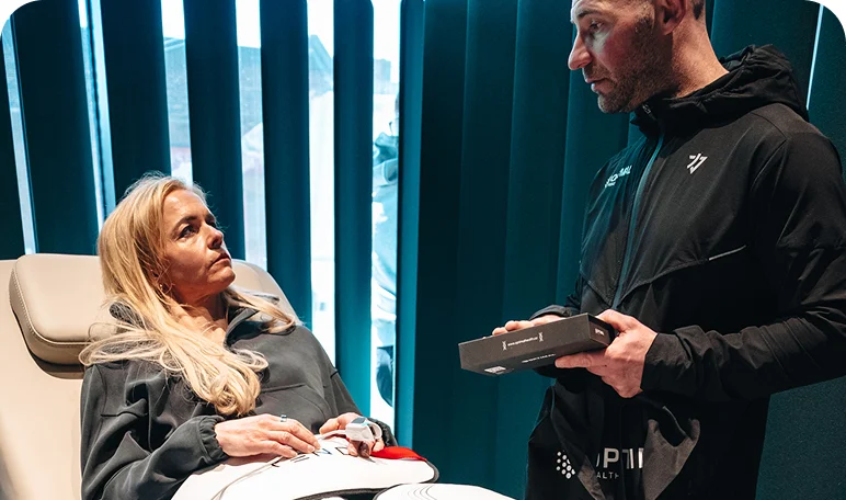 Wellness consultant advising a client on Re:nu London's biohacking treatments as she reclines on a treatment bed.