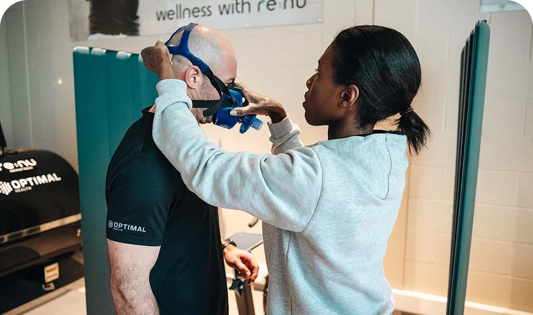 Wellness specialist fitting a breathing mask over a client's head in preparation for a biohacking treatment at Re:nu London.