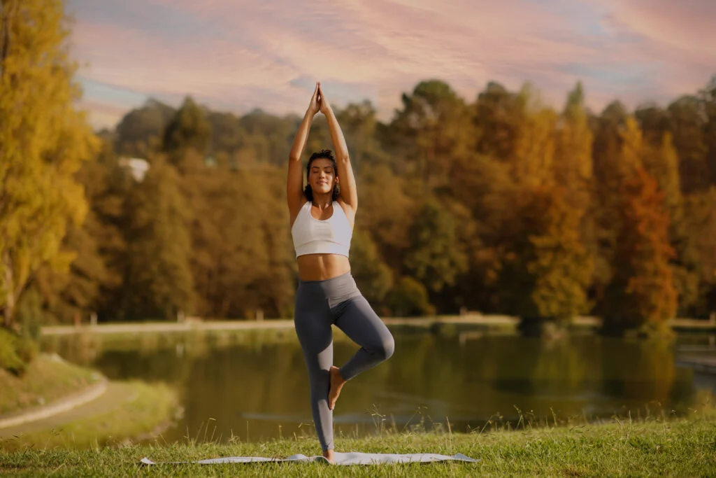 Woman practicing yoga outdoors at sunset by a peaceful lake, surrounded by autumn trees. Promoting balance, mindfulness, and recovery — reflecting Re:nu’s holistic approach to health, wellness, and rejuvenation.