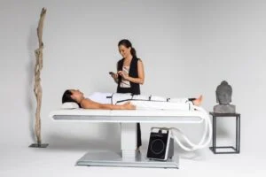A woman lying down on a treatment bed wearing the Stendo compression suit as a wellness specialist monitors the treatment device