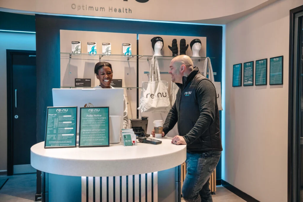 Client speaking with a wellness consultant at the Re:nu Optimum Health reception desk in Greenwich, London.