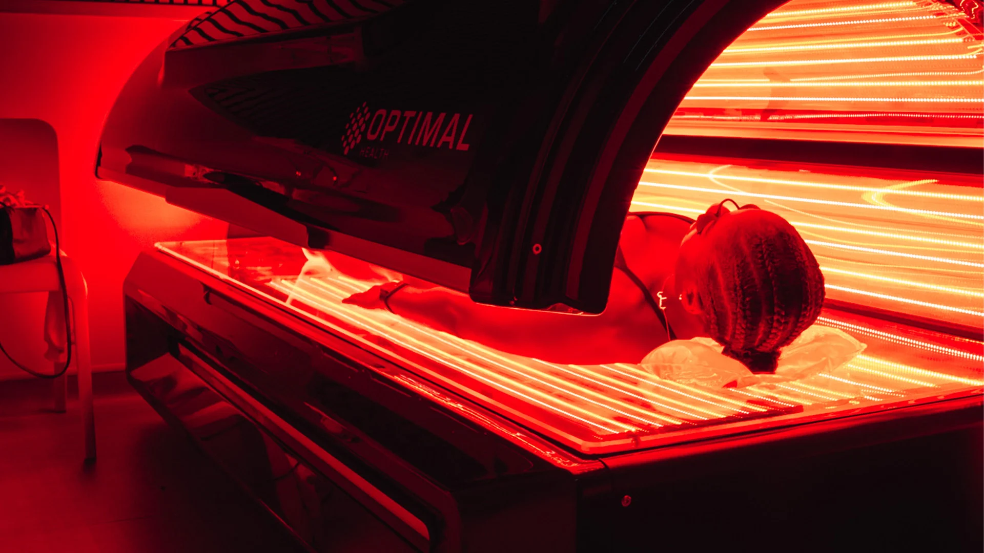 Woman lying down in a Re:nu red light therapy bed emitting red light throughout the room