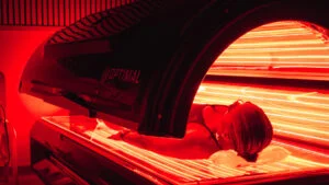 Woman lying in a Re:nu red light therapy chamber emitting a warm red glow.