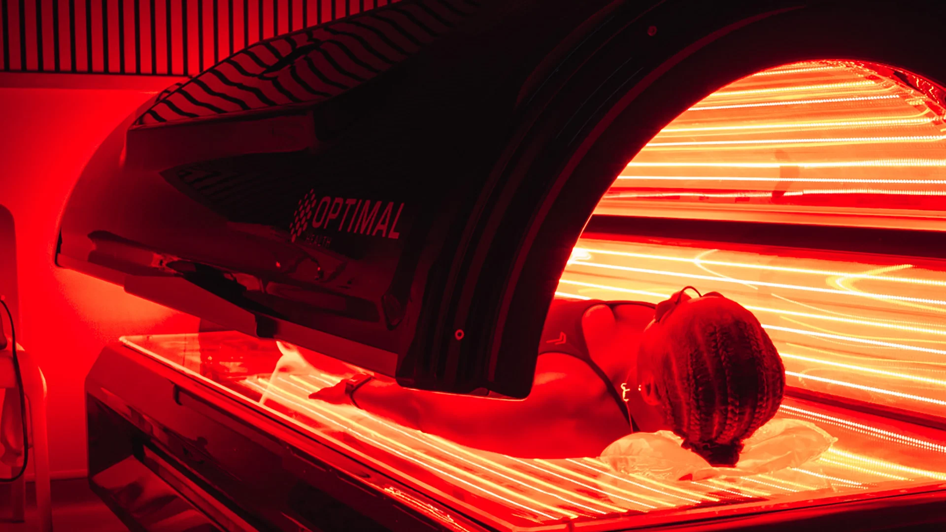 Woman lying in a Re:nu red light therapy chamber emitting a warm red glow.
