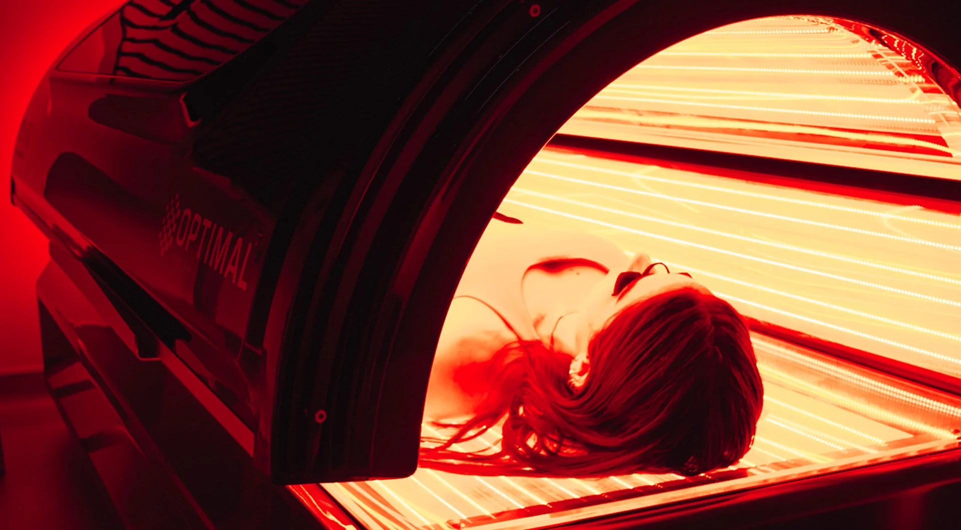 Woman lying down in a full-body red light therapy bed wearing protective eyewear.