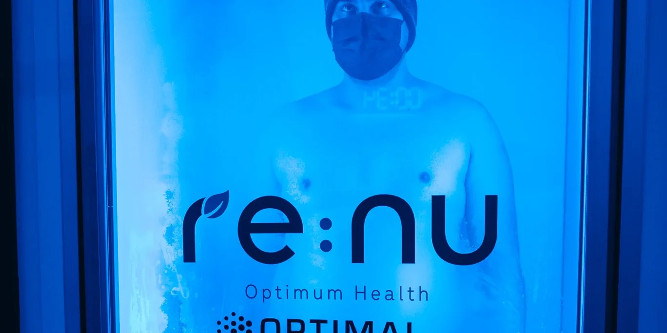 Man standing in a Re:nu Optimum Health cryotherapy chamber wearing a face mask, hat, and gloves