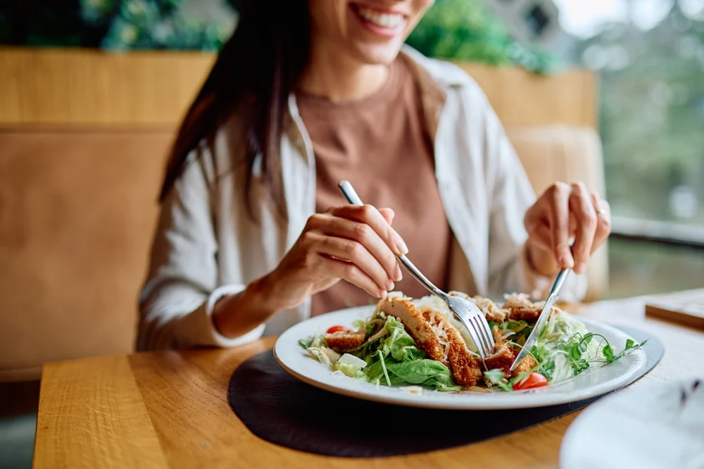 Woman,smiling,,eating,fresh,chicken,salad,in,a,restaurant.,promoting