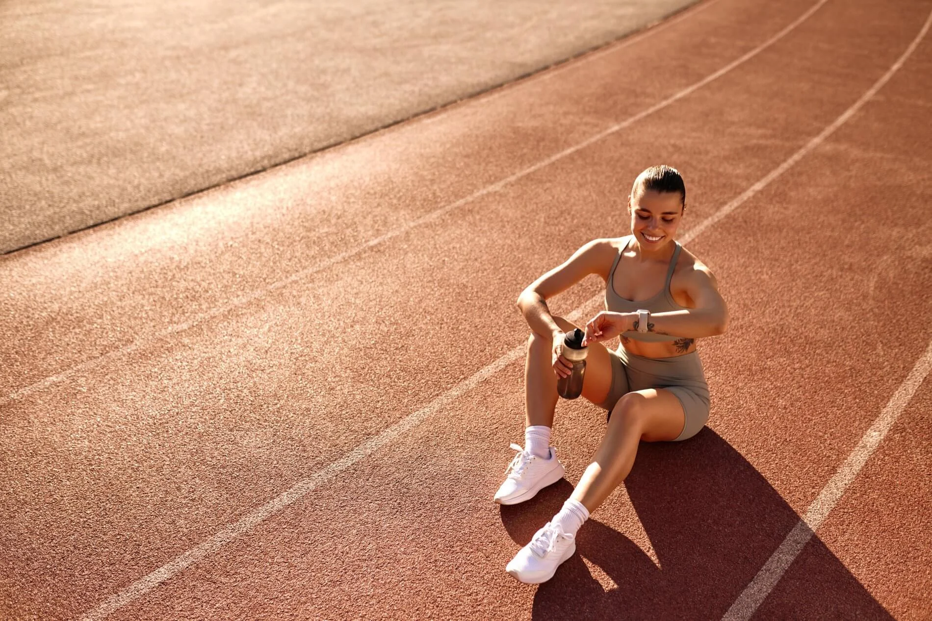 Athletic woman taking a hydration break during recovery on an outdoor running track in London Athletic woman taking a hydration break during recovery on an outdoor running track in London