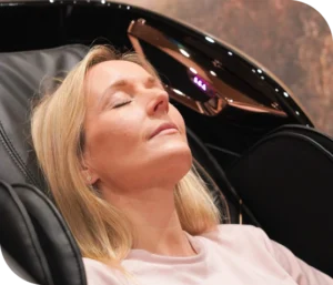 Woman relaxing with eyes closed in Re:nu's massage chair, head supported by the black and rose-gold headrest.